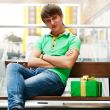 Portrait of young man inside shopping mall with gift box sitting