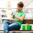 Portrait of young man inside shopping mall with gift box sitting