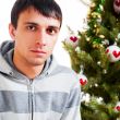 Young calm man sitting in front of Christmas tree