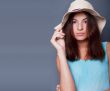 Confident woman with arms near her head holding hat against a bl