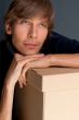 Portrait of young man leaning on box against grey wall. He is st