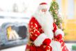 Santa sitting at the Christmas tree, near fireplace and looking 