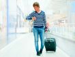 Portrait of young man walking inside modern airport with trolley