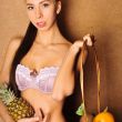 Portrait of young sexy woman holding fruit in her arms, standing