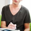 Young adult man writing in his copybook while sitting on a large