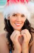 Young beautiful woman wearing christmas hat showing heart shape 