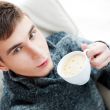 Portrait of a young man drinking coffee while sitting on armchai