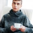 Portrait of a young man drinking coffee while sitting on armchai