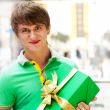 Portrait of young man inside shopping mall with gift box sitting