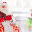 Santa sitting at the Christmas tree, near fireplace and reading 