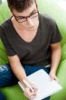 Young adult man writing in his copybook while sitting on a large