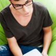 Young adult man writing in his copybook while sitting on a large
