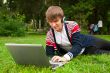 Student laying on grass and using laptop outside school