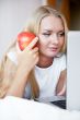 Smiling woman using a laptop while lying on her bed and eating r