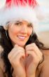 Young beautiful woman wearing christmas hat showing heart shape 