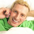 A man in his bed speaking cell phone and looking at camera