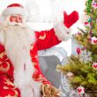 Santa sitting at the Christmas tree, near fireplace and looking 