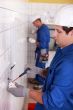 Pair of electricians wiring a white tiled room