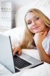 Smiling woman using a laptop while lying on her bed