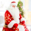 Santa sitting at the Christmas tree, near fireplace and looking 