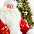 Santa sitting at the Christmas tree, fireplace and looking at ca