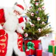 Santa sitting at the Christmas tree, fireplace and looking at ca