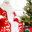 Santa sitting at the Christmas tree, fireplace and looking at ca