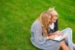 Portrait of two smiling women using laptop on a green meadow at 