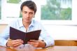 Portrait of a young handsome man with a book indoors