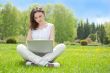 Young woman with laptop sitting on green gras