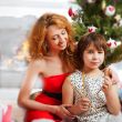 Mother and her daughter sitting together near christmas tree