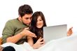 Portrait of a happy young couple looking at the screen while usi