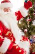 Santa sitting at the Christmas tree, near fireplace and looking 