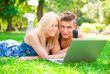 Portrait of young couple outdoor resting on green grass and usin
