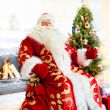 Santa sitting at the Christmas tree, fireplace and looking at ca