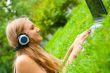 A smiling young girl with laptop outdoors listening music by hea