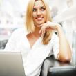 Portrait of happy blond woman using laptop at shopping mall cafe