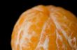 Close up photograph of a peeled Clementine orange on a black bac
