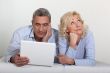 Middle aged couple with a laptop on their bed.