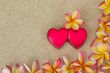 Frangipani /plumeria flower frame, with two red hearts on sand