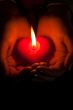 Human hands hold heart shaped burning candle