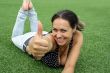 young woman lying on green meadow and shows up finger