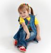little girl in jeans and sandals is sitting on the floor