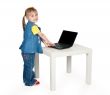 little girl in blue jeans standing at a table with a laptop