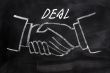 Business deal written on a blackboard background with handshaking
