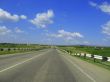 Wide highway and meadow. Clouds over and blue sky