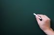 Blackboard background with a hand holding chalk writing.
