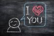 Speech bubble with a cartoon figure, saying I love you drawn on a blackboard background