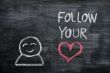 Speech bubble with a cartoon figure and the phrase `Follow your heart` drawn on a blackboard background