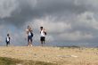 Several people are on top of the mountain against the dark clouds. 
